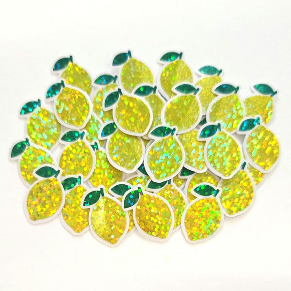 May include: A collection of yellow lemon-shaped sticker embellishments with green leaves. The lemons are sparkly with green leaf and clear borders.