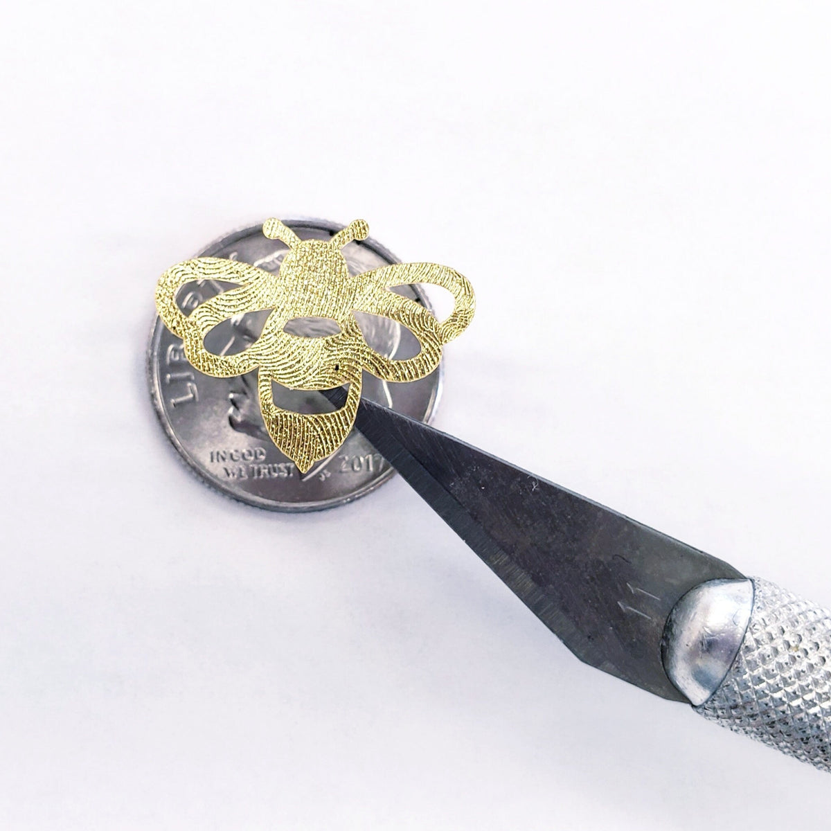 A gold bee sticker with a craft knife on top of a US quarter coin for scale.
