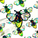 Close-up of iridescent glitter firefly stickers with black outlines. The lightning bugs have a black and yellow body and iridescent wings. Handmade stickers